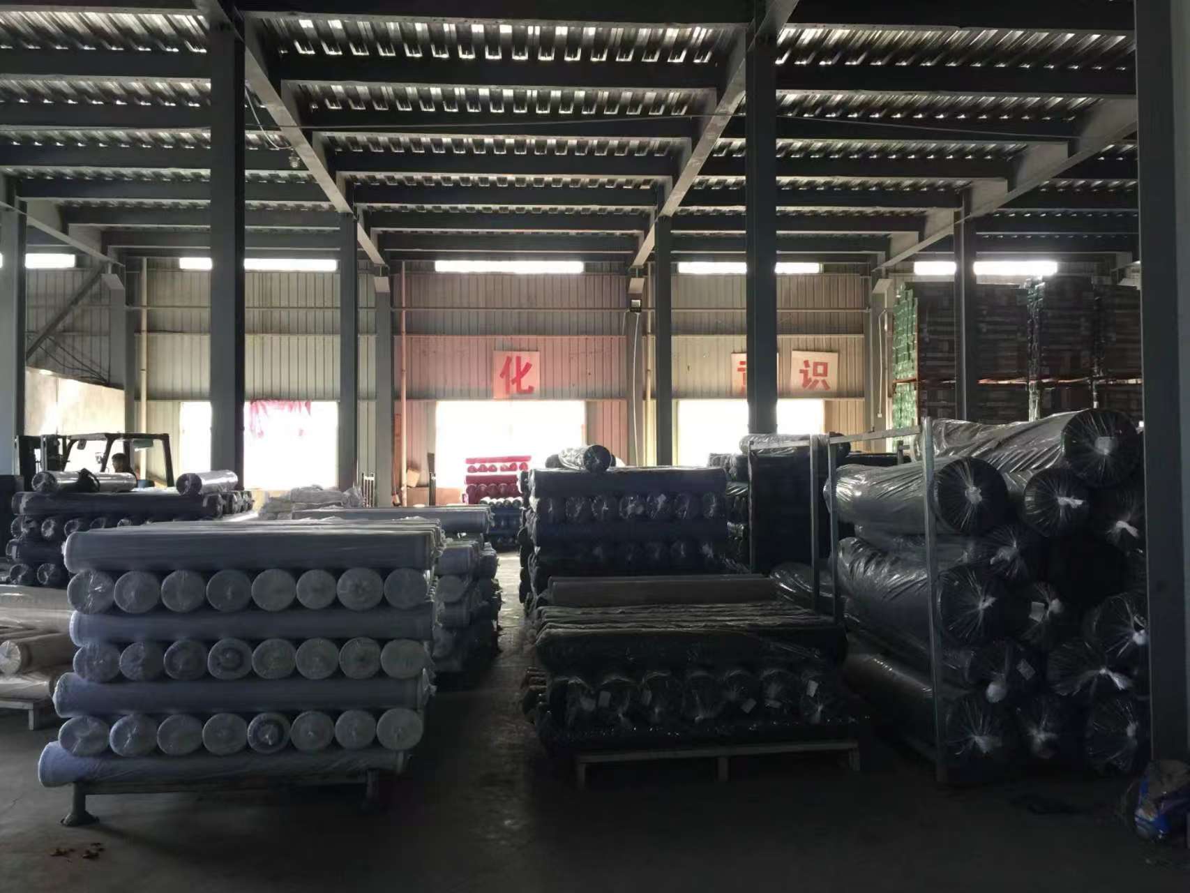 Stacks of metal tubes and large fabric rolls organized in a warehouse